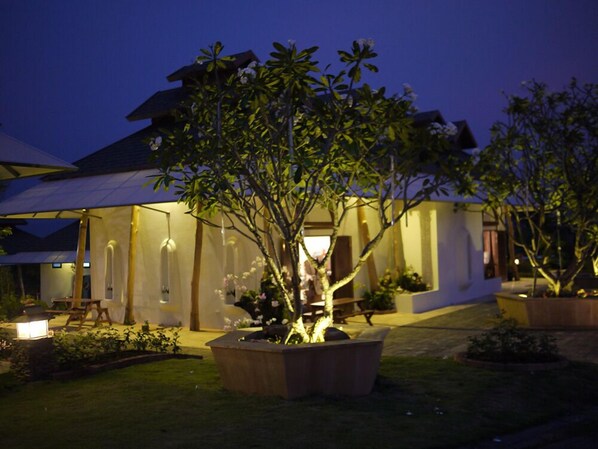 A modern house with a covered outdoor area, large potted plants, and a well-lit garden at dusk. - Phukumhom (Pak Chong)
