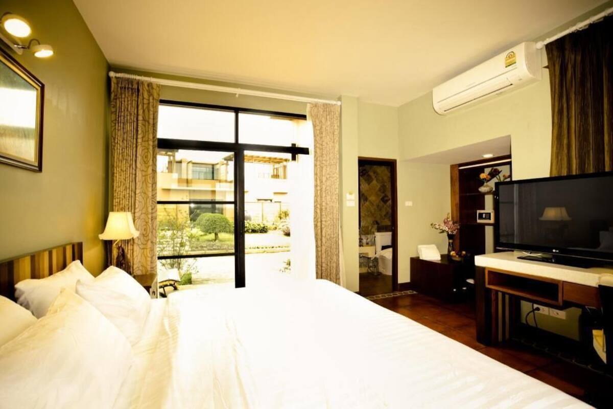 A hotel room with a bed, a television, an air conditioning unit, and a view of the outside.