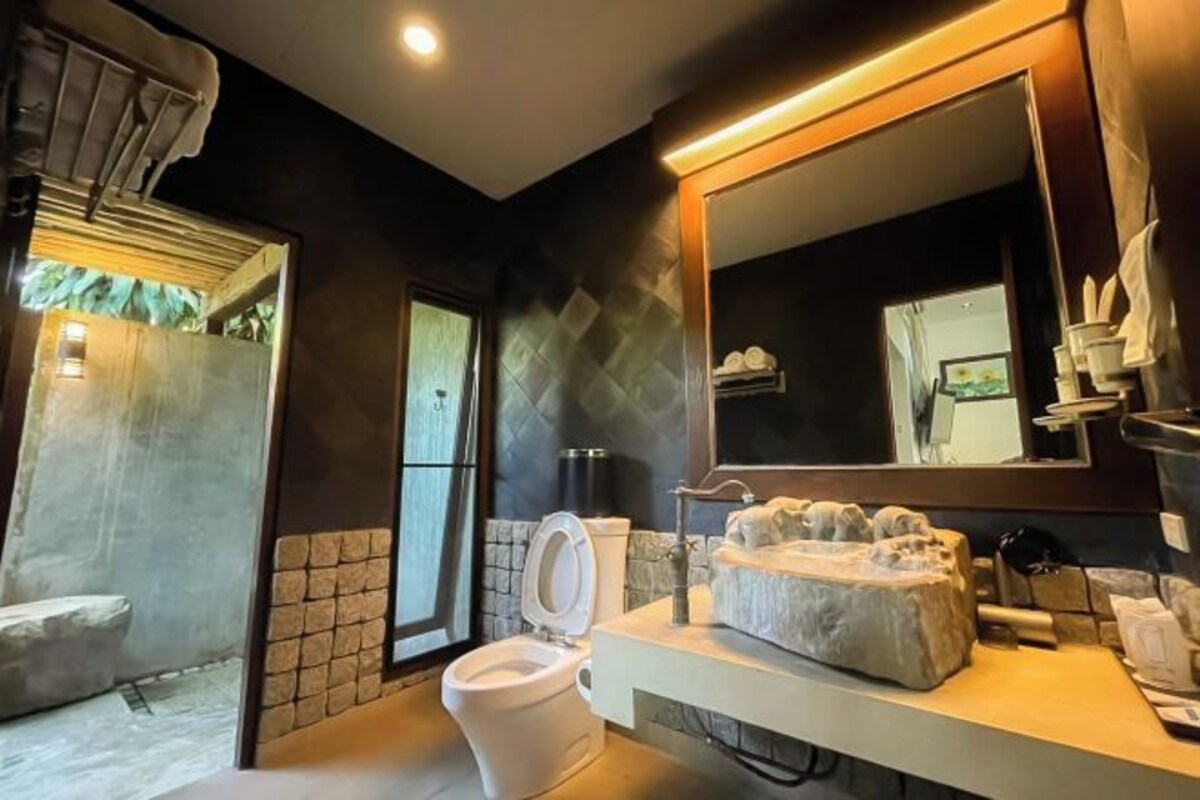 Un baño moderno con pared de piedra, un espejo grande, un inodoro blanco y un lavabo de mármol.