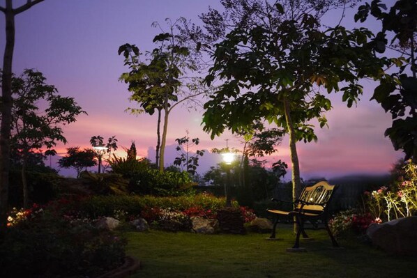 Un jardín al atardecer con un banco y un farol.