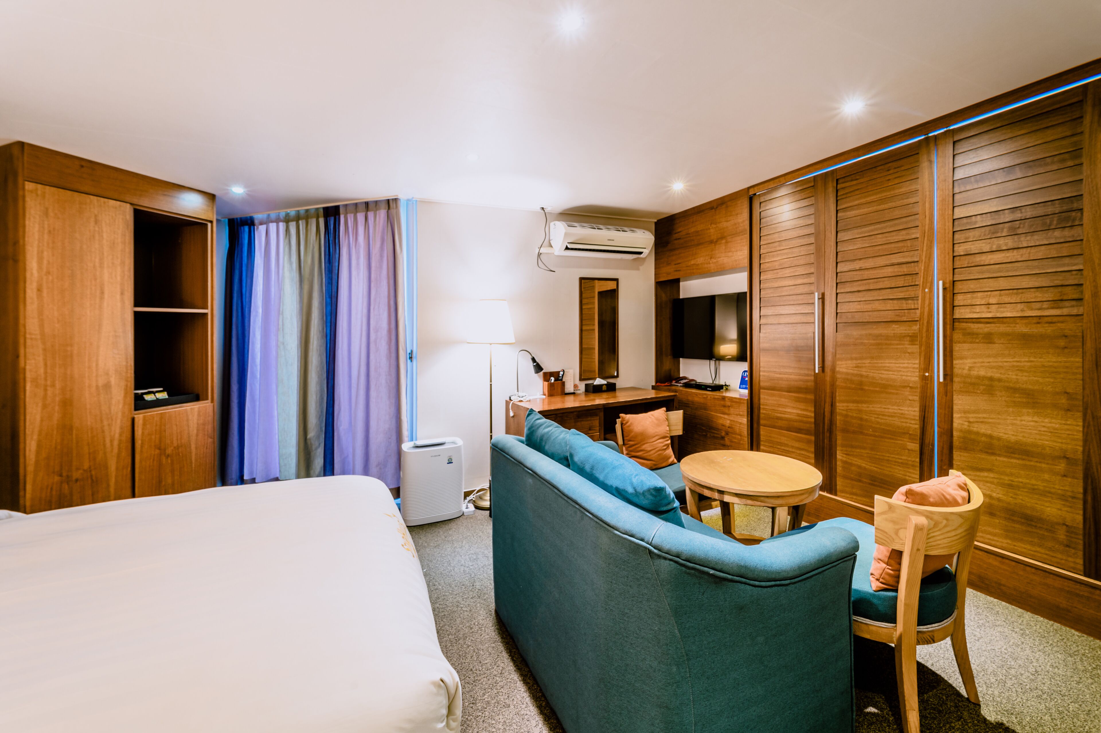Habitación de hotel con cama, sofá, mesita, silla, escritorio y armario.