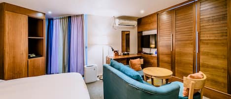 Habitación de hotel con cama, sofá, mesita, silla, escritorio y armario.