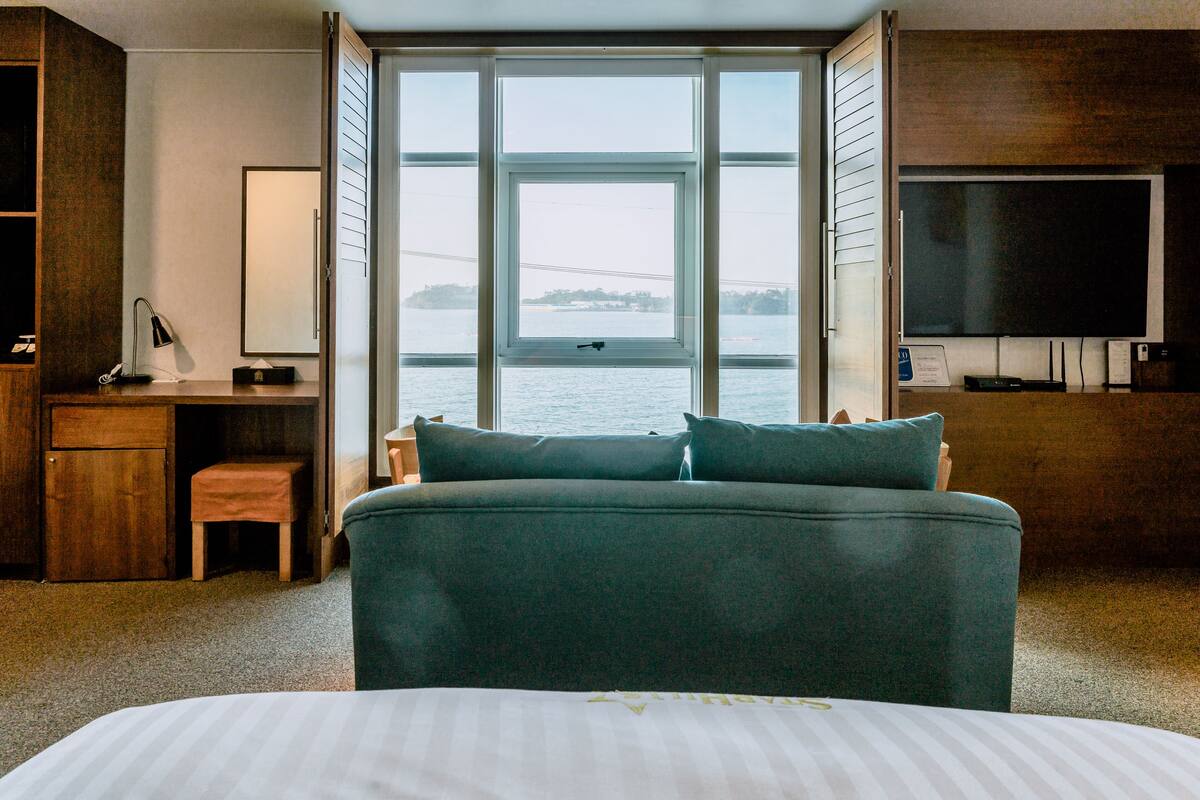 A bedroom with a large bed, a desk, a chair, a television, and a view of the water.