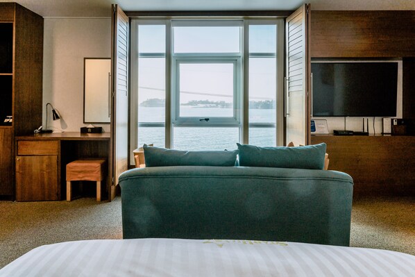 Une chambre avec un grand lit, un bureau, une chaise, une télévision et une vue sur l’eau.