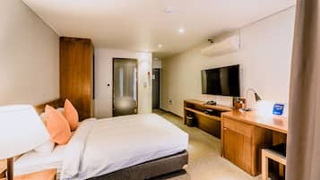 A hotel room with a bed, bedside table, lamp, TV, desk, and a small cabinet.