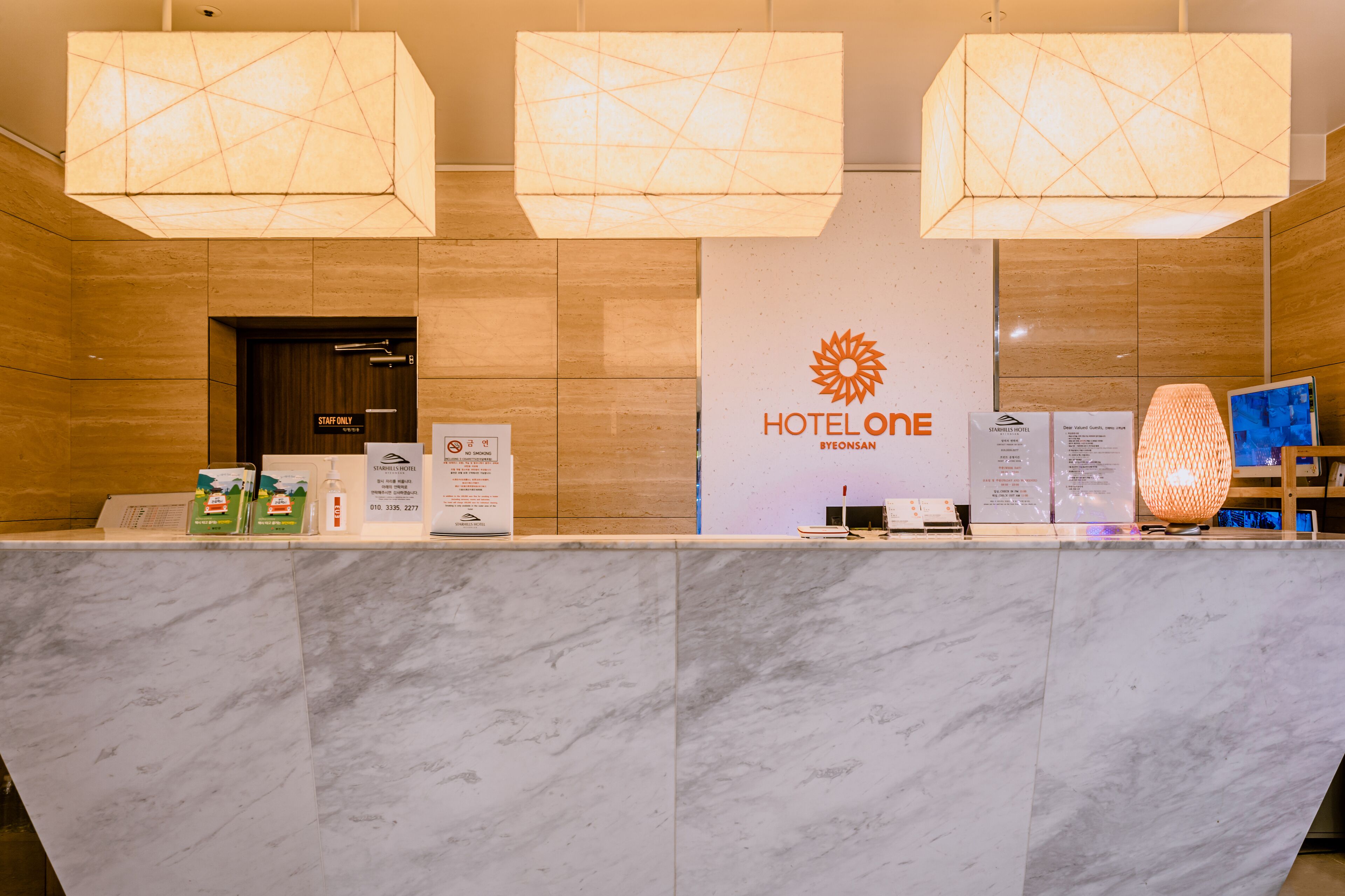 A hotel reception desk with a marble counter, three geometric pendant lights, and a sign reading "HOTELONE RYONSAN".