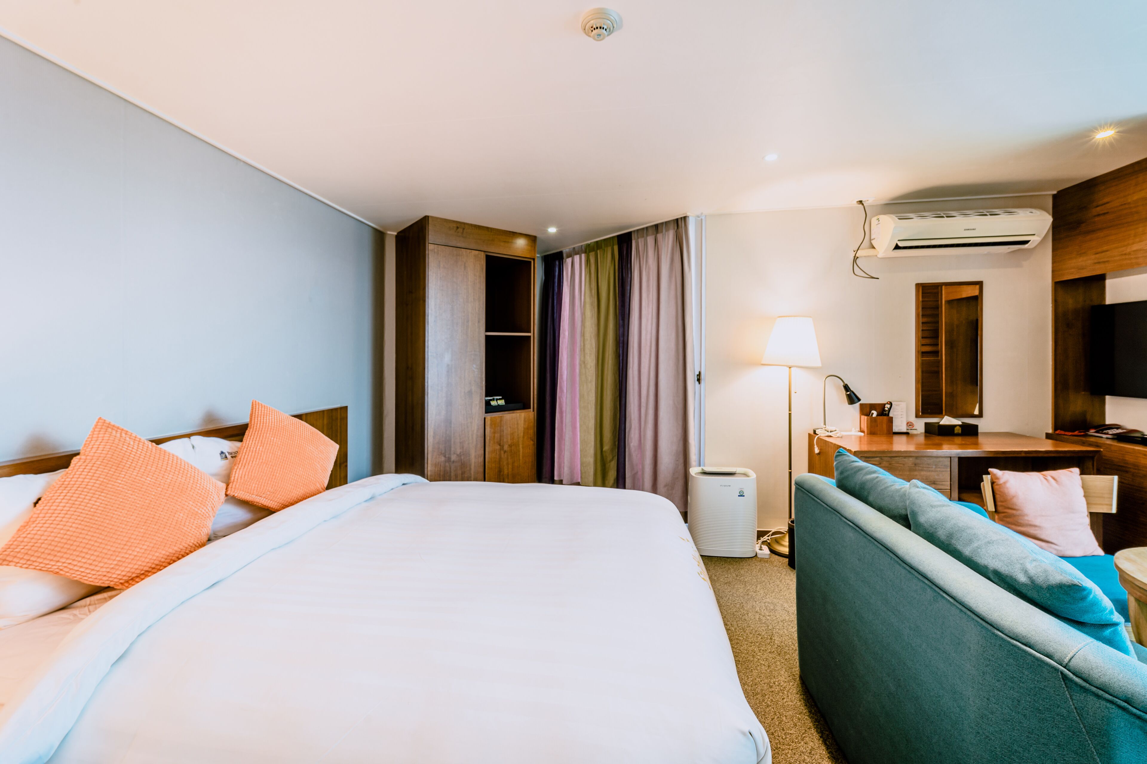 Ein Hotelzimmer mit einem großen Bett, einer Sitzecke, einem Schreibtisch mit Lampe, einer Klimaanlage und einem Kleiderschrank.