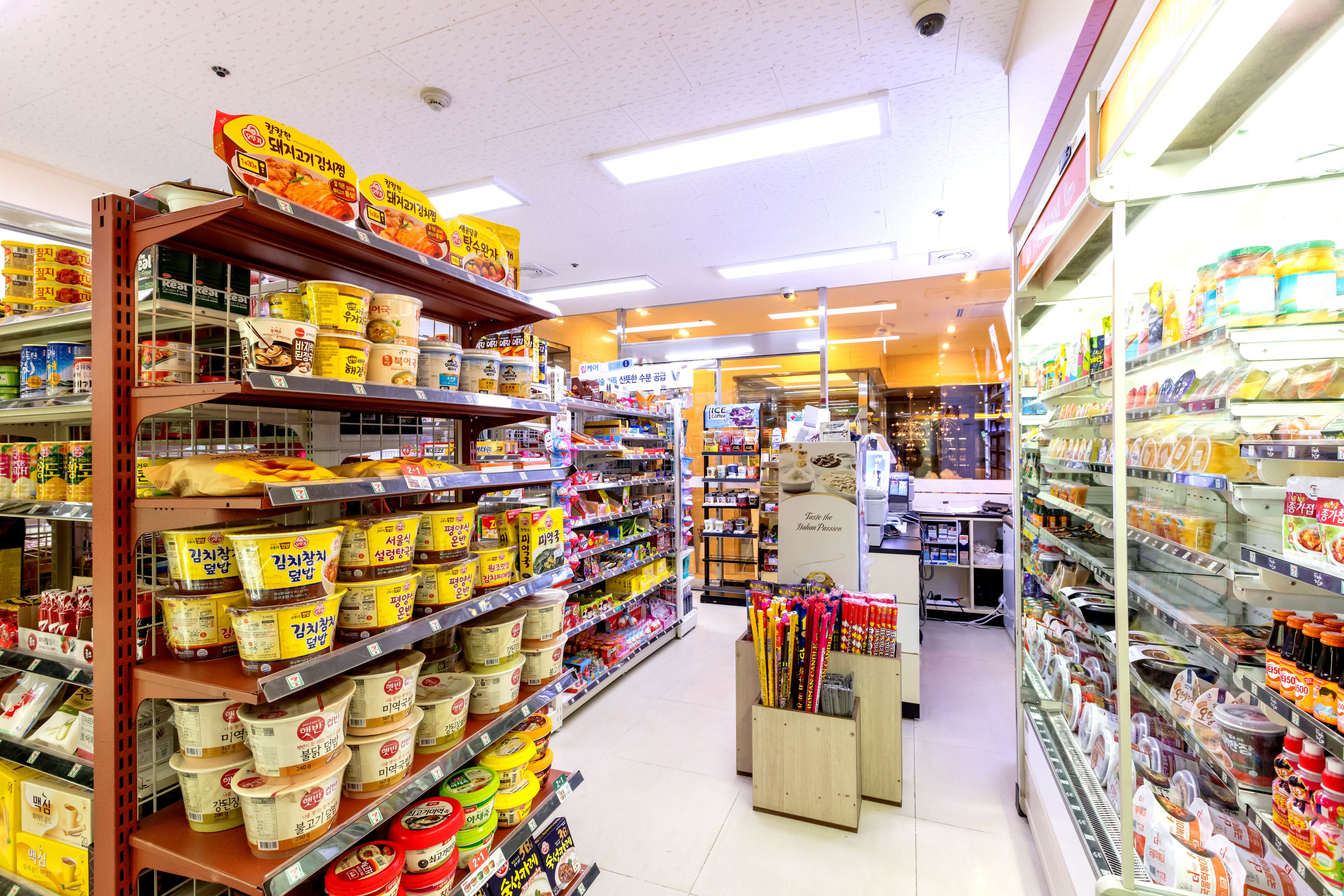 Un pasillo de supermercado con estantes llenos de diversos productos alimenticios y una sección refrigerada a la derecha.