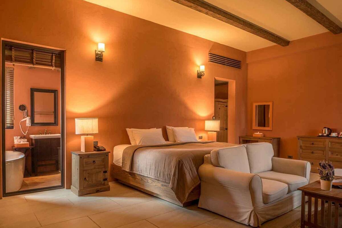 Un dormitorio con una cama, dos mesitas de noche, un aparador, un sofá, un espejo y un cómoda.