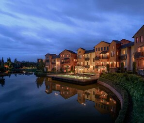 Un hotel frente al agua con varias construcciones, un estanque reflectante y balcones bien iluminados.