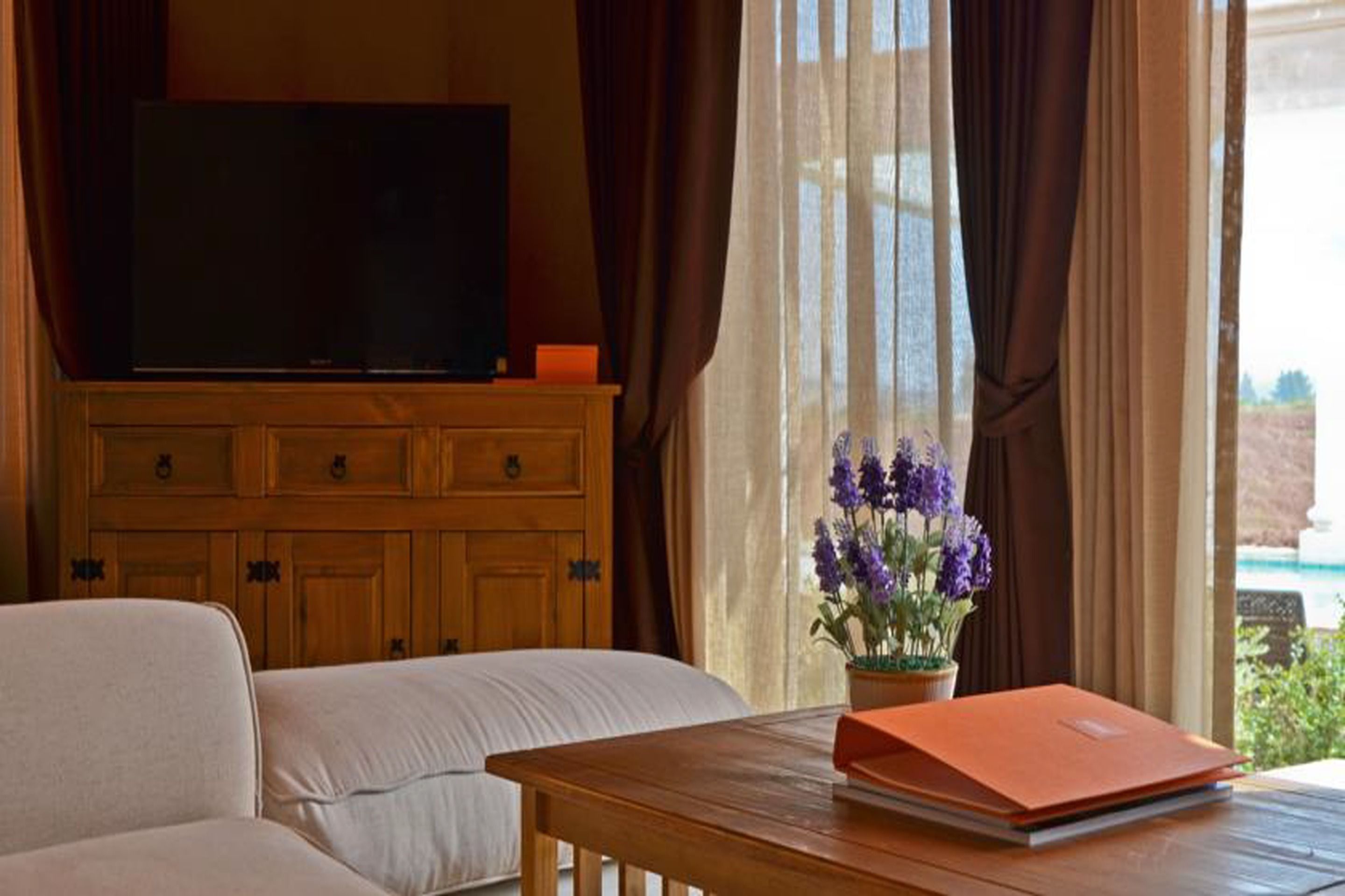 A living room with a sofa, a wooden cabinet, a television, and a table with a flower vase and a book.