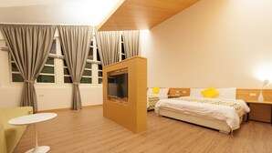 Ett modernt hotellrum med trägolv, en säng med vita sängkläder och en gul kudde, ett litet runt bord och en tv som är monterad på ett träskåp.