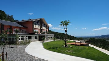 A modern two-story building with a large glass facade, a curved driveway, and a well-maintained lawn.