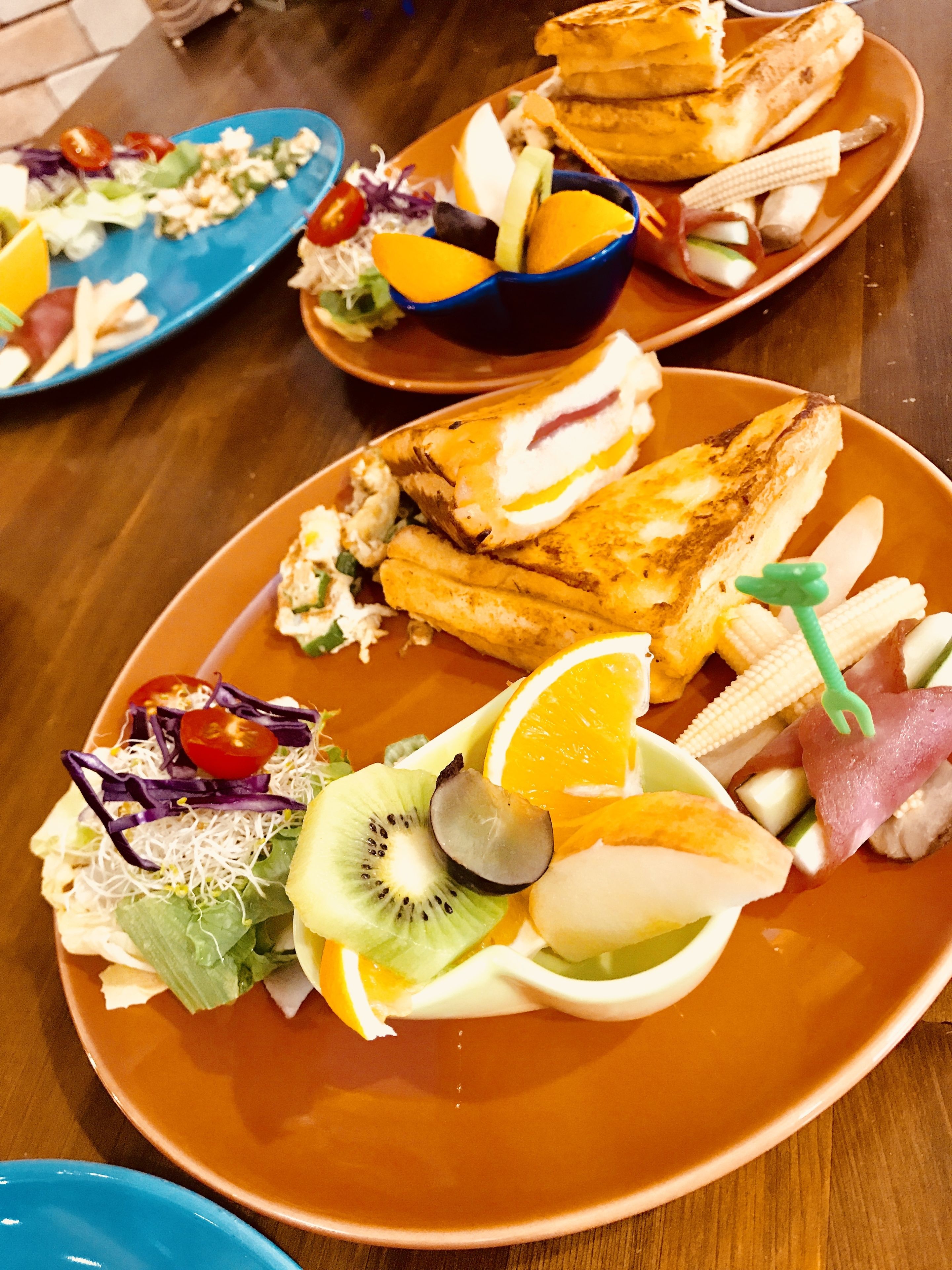 Une table sur laquelle on trouve différents plats, notamment des sandwichs, des salades et des fruits.