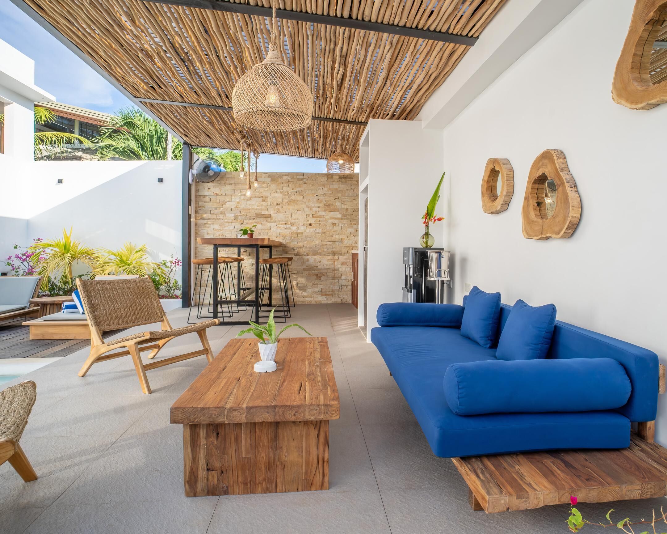 Uma área externa moderna com mesa de centro de madeira, sofá azul, cadeiras de vime e uma mesa de jantar.