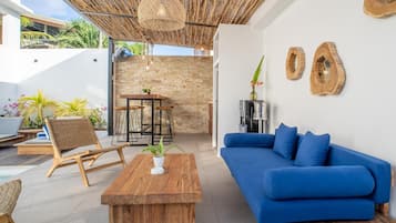Un espacio al aire libre moderno con una mesa de centro de madera, sofá azul, sillas de mimbre y una mesa de comedor.