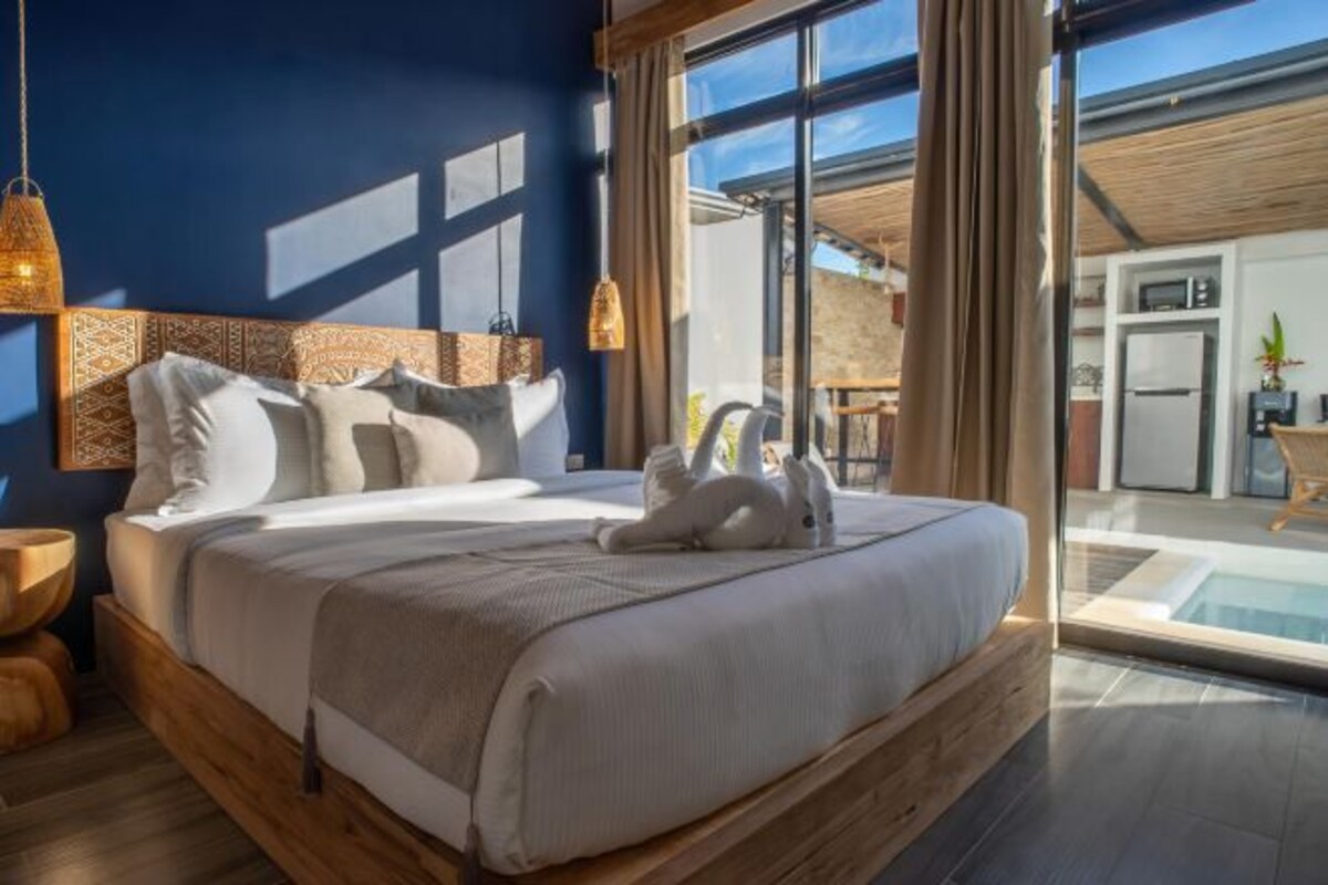 A modern bedroom with a large bed, wooden headboard, and a view of a pool and outdoor area.