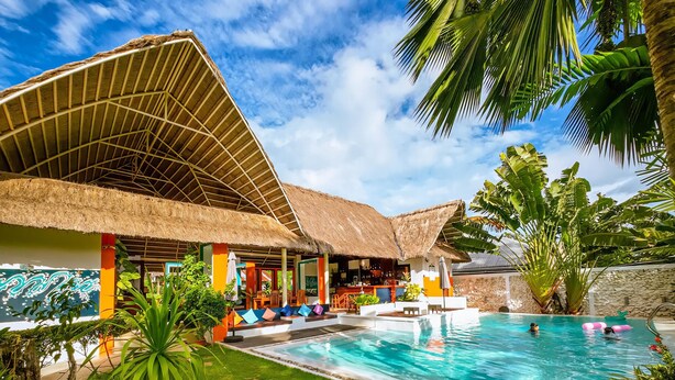 A pool area with a thatched-roof structure, a grassy lawn, and palm trees. - Villa Kasadya (Panglao)