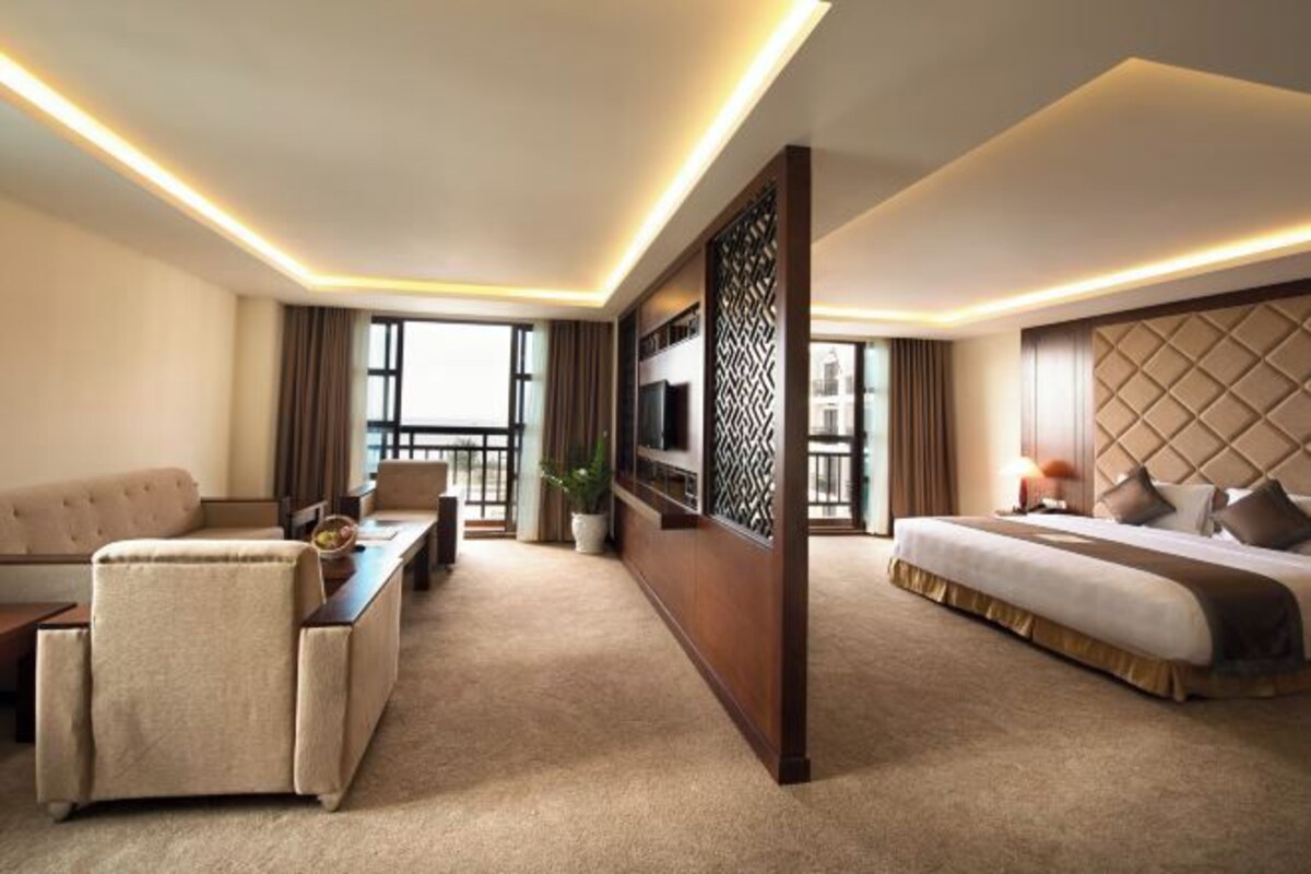 Una habitación de hotel moderna con sofá, cama, televisión y un ventanal grande.