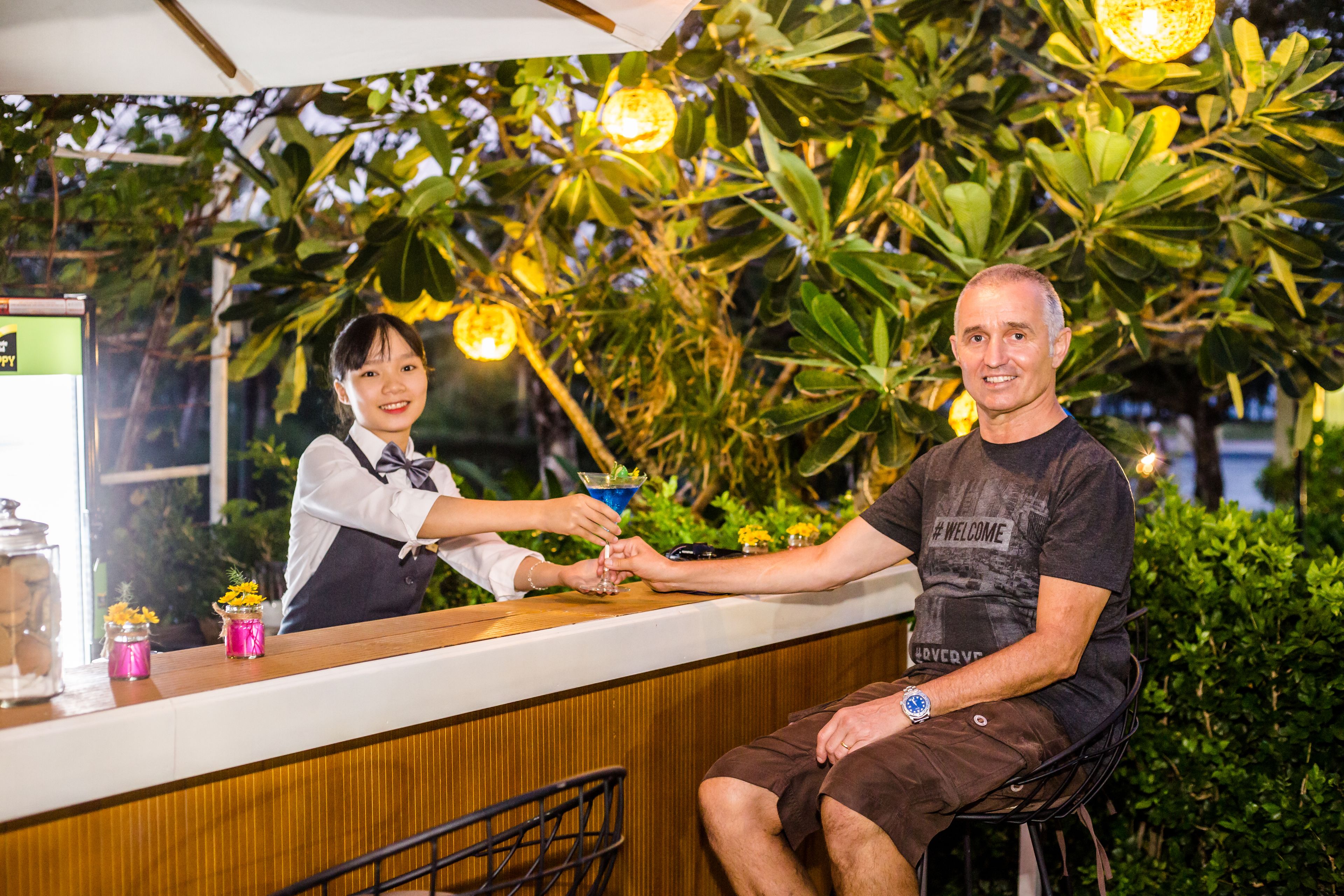 A bar area with a counter, a person seated, and another person standing behind the counter.