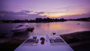 Une table dressée pour deux personnes, avec des verres à vin et une rose, donnant sur une étendue d'eau calme au crépuscule.