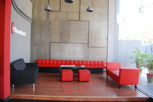 Un vestíbulo moderno con un sofá rojo, un sillón negro y otomanas rojas. Hay un banco a lo largo de la pared y una planta en maceta en la esquina.