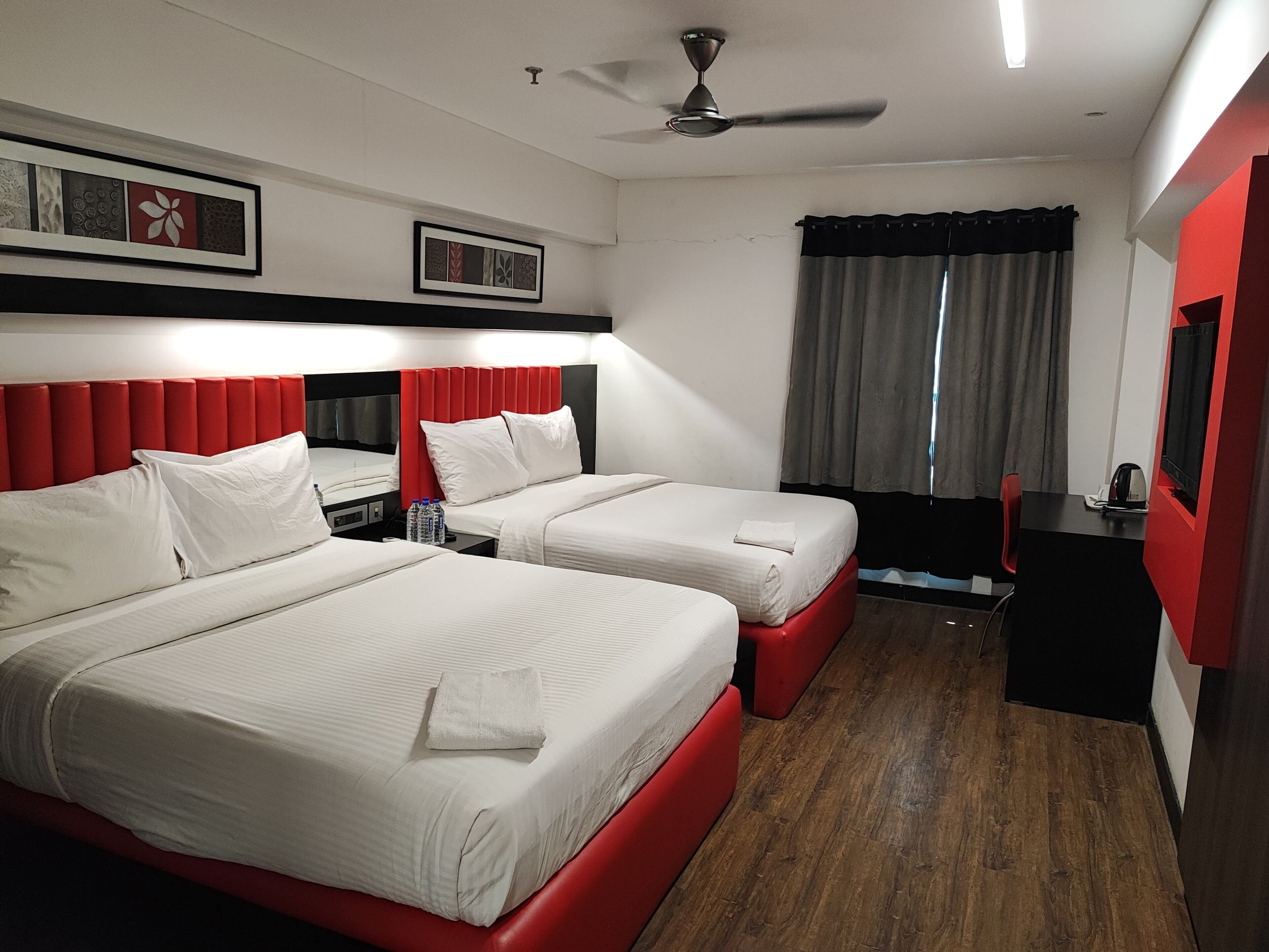 A hotel room with two beds, a desk, a chair, a TV, and a ceiling fan.