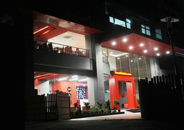 Een modern hotel met een gevel in rood en wit, een glazen ingang en een zichtbaar balkon op de bovenverdieping.