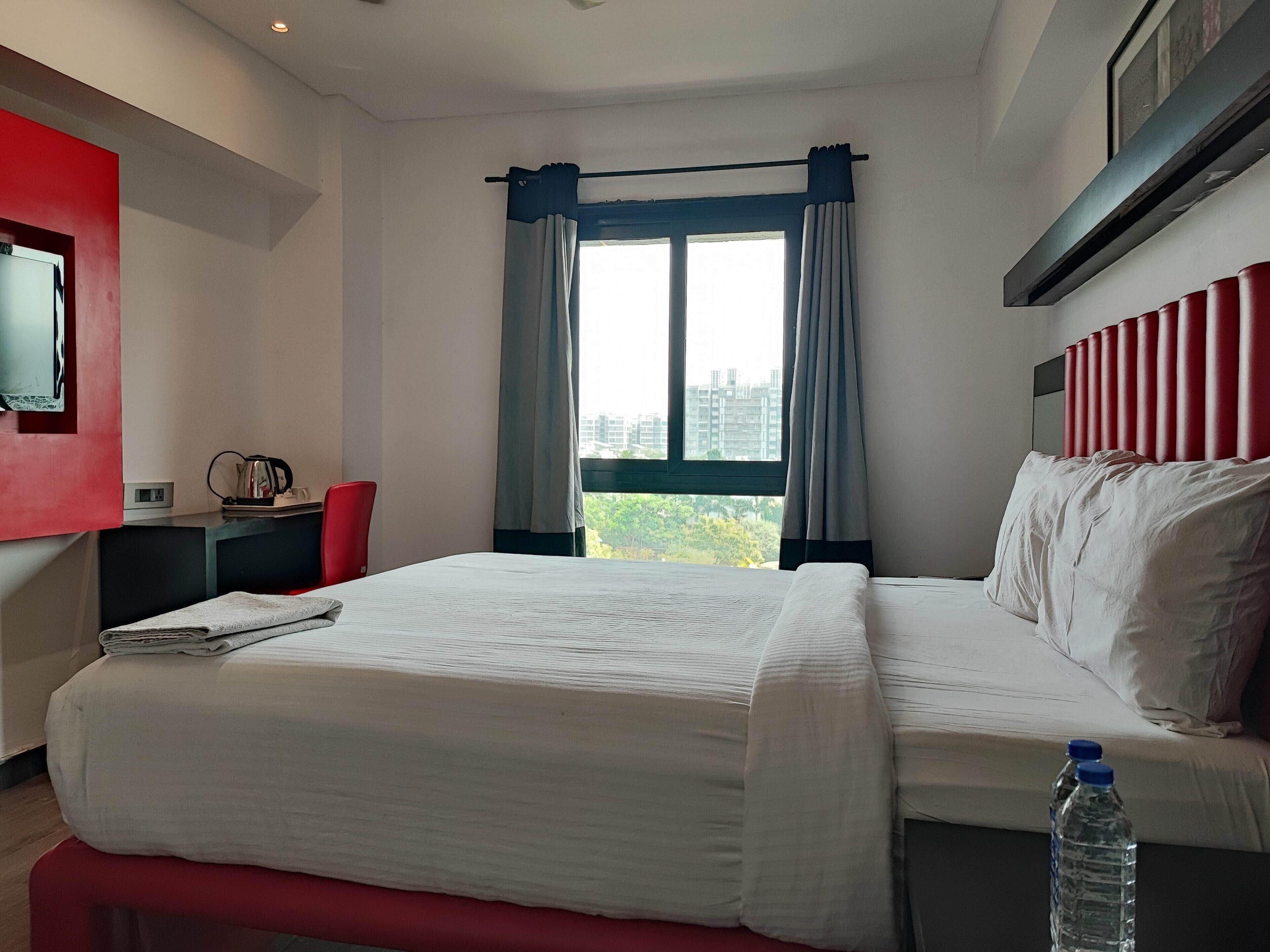 A hotel room with a bed, a desk, a chair, a window with curtains, and a city view.