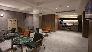 Ett modernt hotellrum med ett litet kök, sittgrupp med bord och en stor spegel.