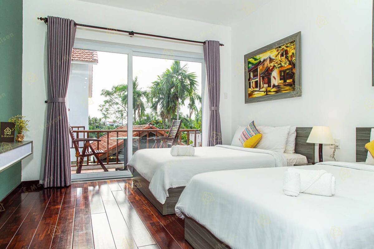 A hotel room with two beds, a balcony with a view of palm trees, and a painting on the wall.