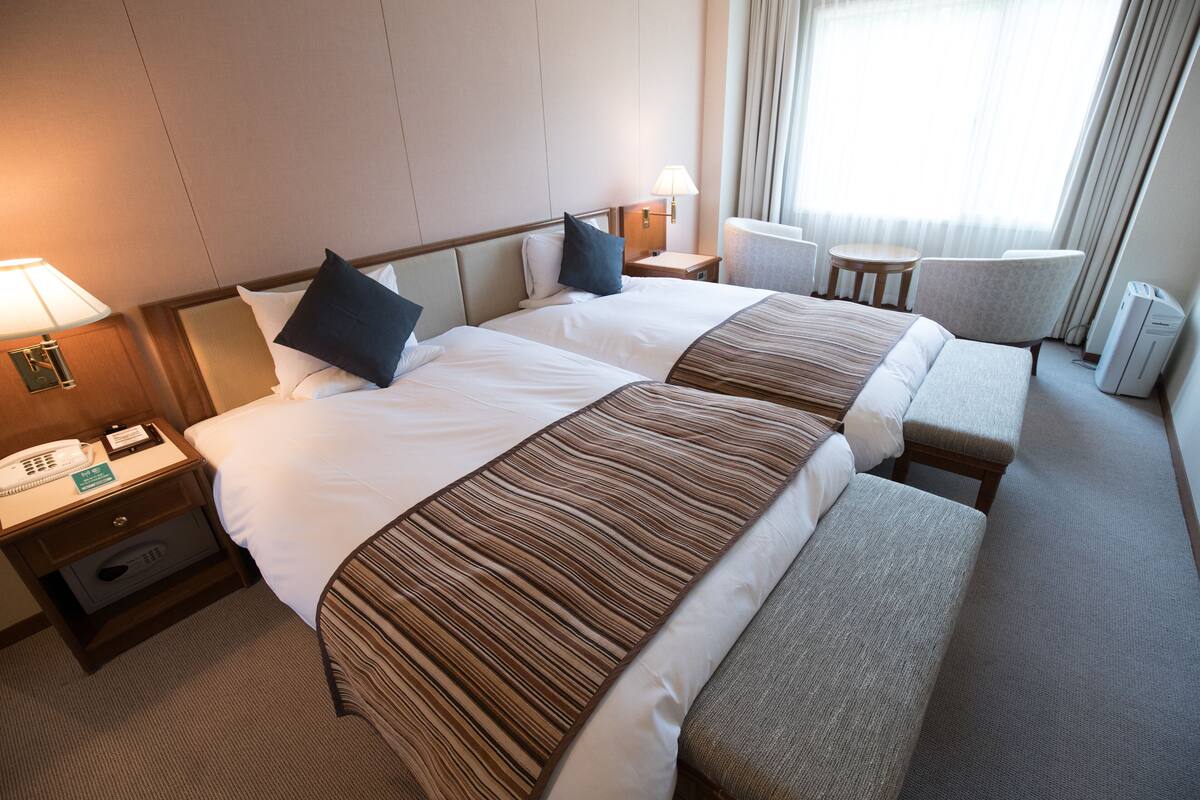 Una habitación de hotel con dos camas, una zona de estar, una mesita y una lámpara.