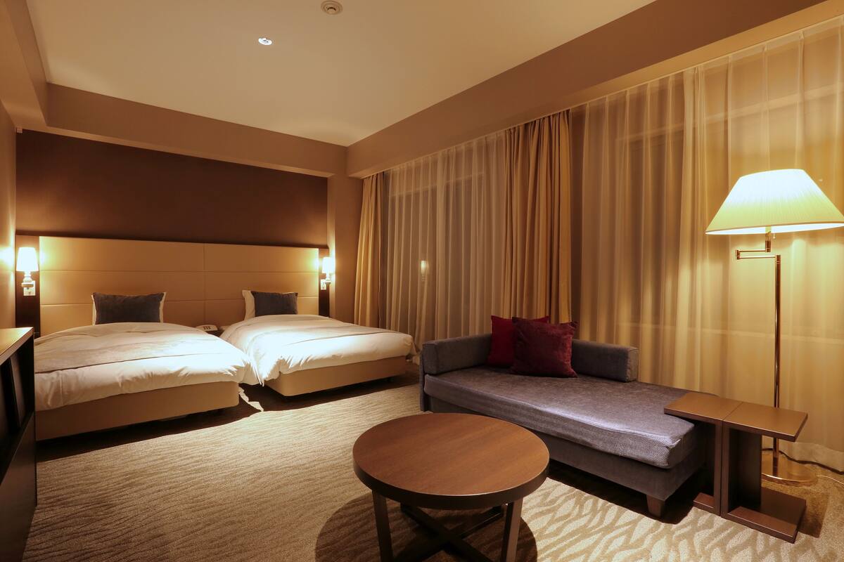 Habitación de hotel con dos camas, un sofá, una mesita de centro redonda y una lámpara.