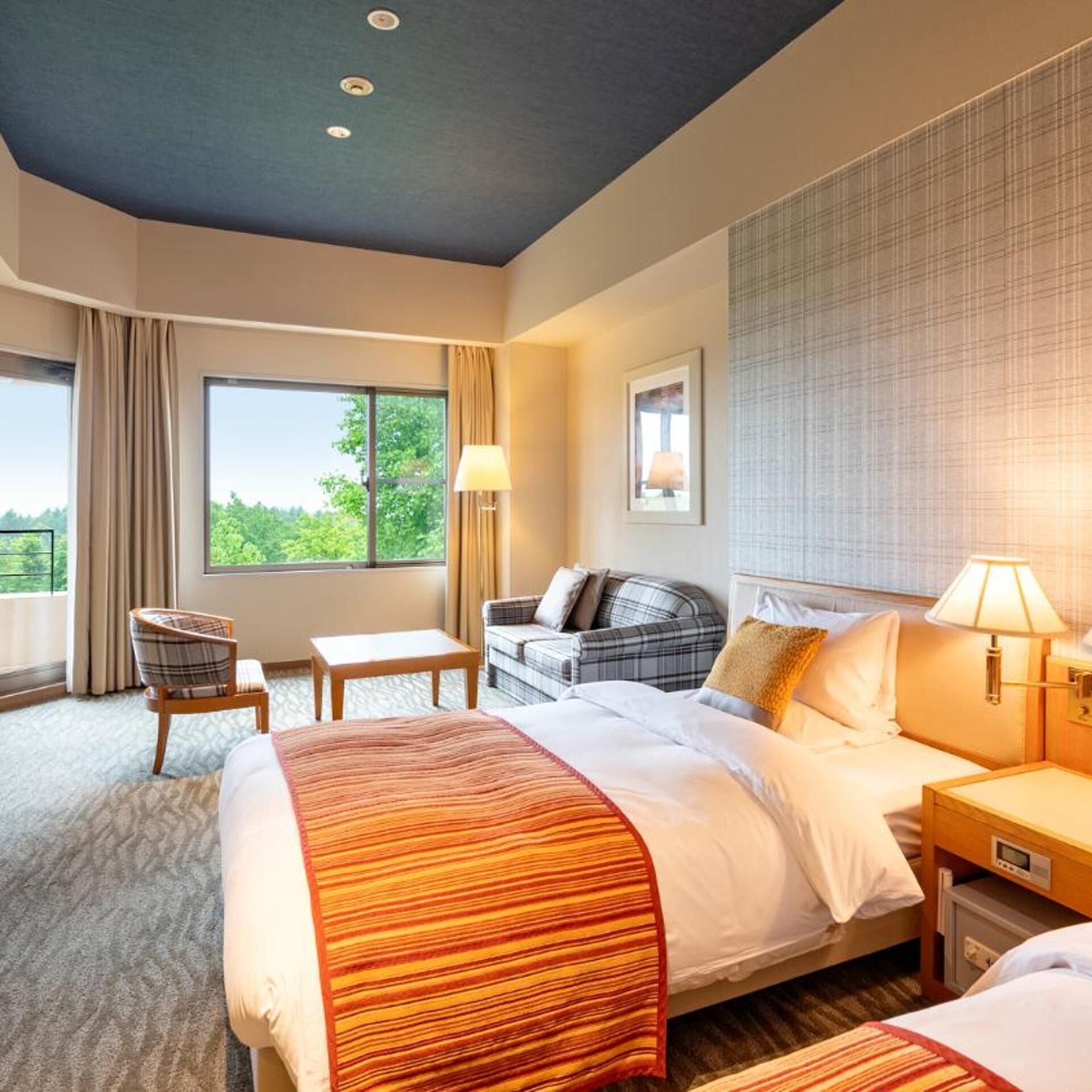 A hotel room with a large bed, a sofa, a chair, a small table, and a window with curtains.