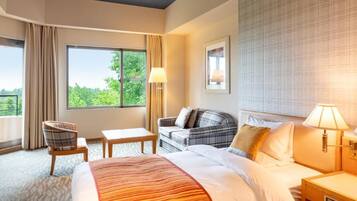 A hotel room with a large bed, a sofa, a chair, a small table, and a window with curtains.
