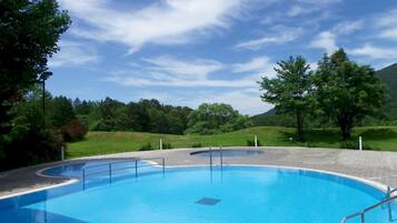 A large, clear blue swimming pool with a curved edge, surrounded by a paved deck and trees.
