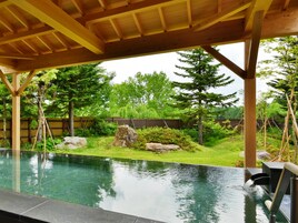 Ein Poolbereich mit einer hölzernen Pergola darüber, umgeben von üppiger Bepflanzung und einem Holzzaun.