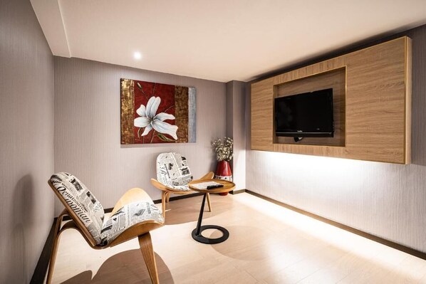 A modern living room with two wooden chairs, a flat-screen TV mounted on the wall, and a large floral artwork. - Global Traveler Hotel Kaohsiung (Kaohsiung)