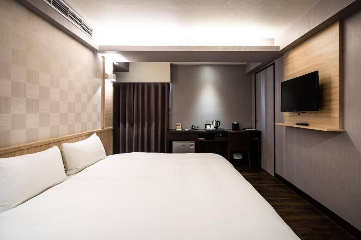 A hotel room with a large bed, a desk with a computer, a flat-screen TV, and a shower area.