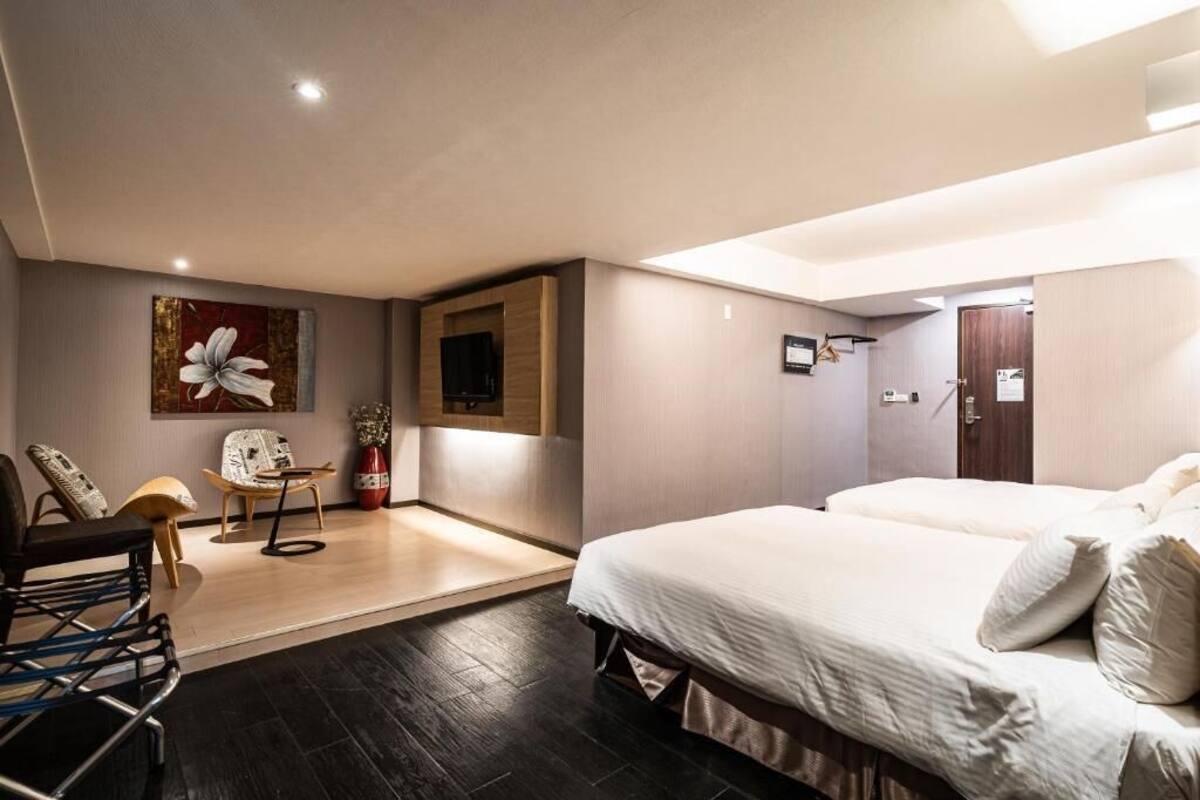 A modern hotel room with a large bed, a seating area with chairs, a flat-screen TV, and a decorative vase.