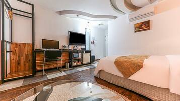 Een moderne hotelkamer met een bed, een bureau met een computer, een televisie en een kleine kitchenette.