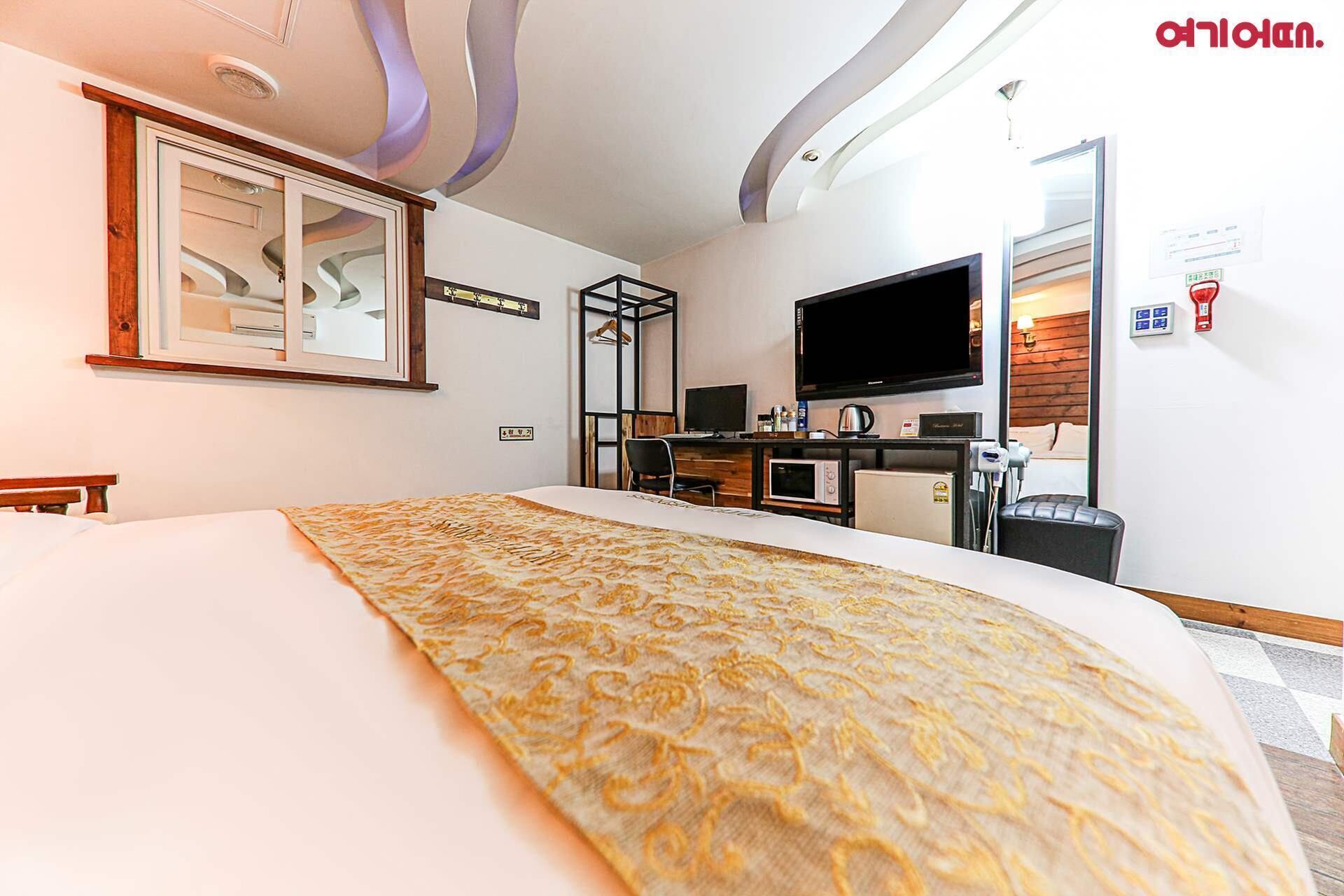A hotel room with a bed, a desk with a computer, a television, and a microwave.