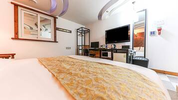 A hotel room with a bed, a desk with a computer, a television, and a microwave.