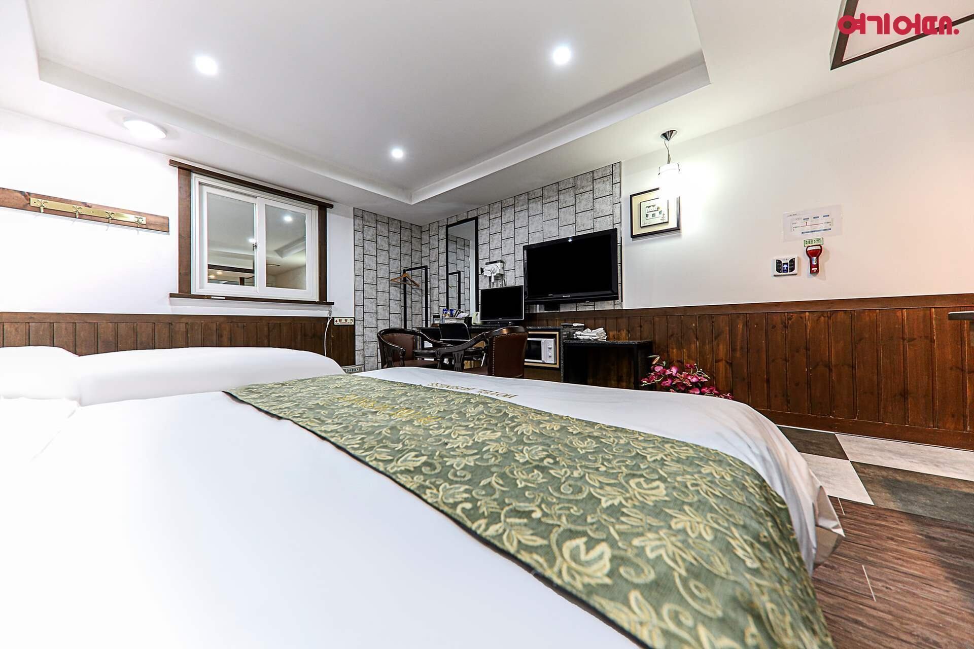 Ett hotellrum med två sängar, ett skrivbord, en stol, en tv och ett fönster.