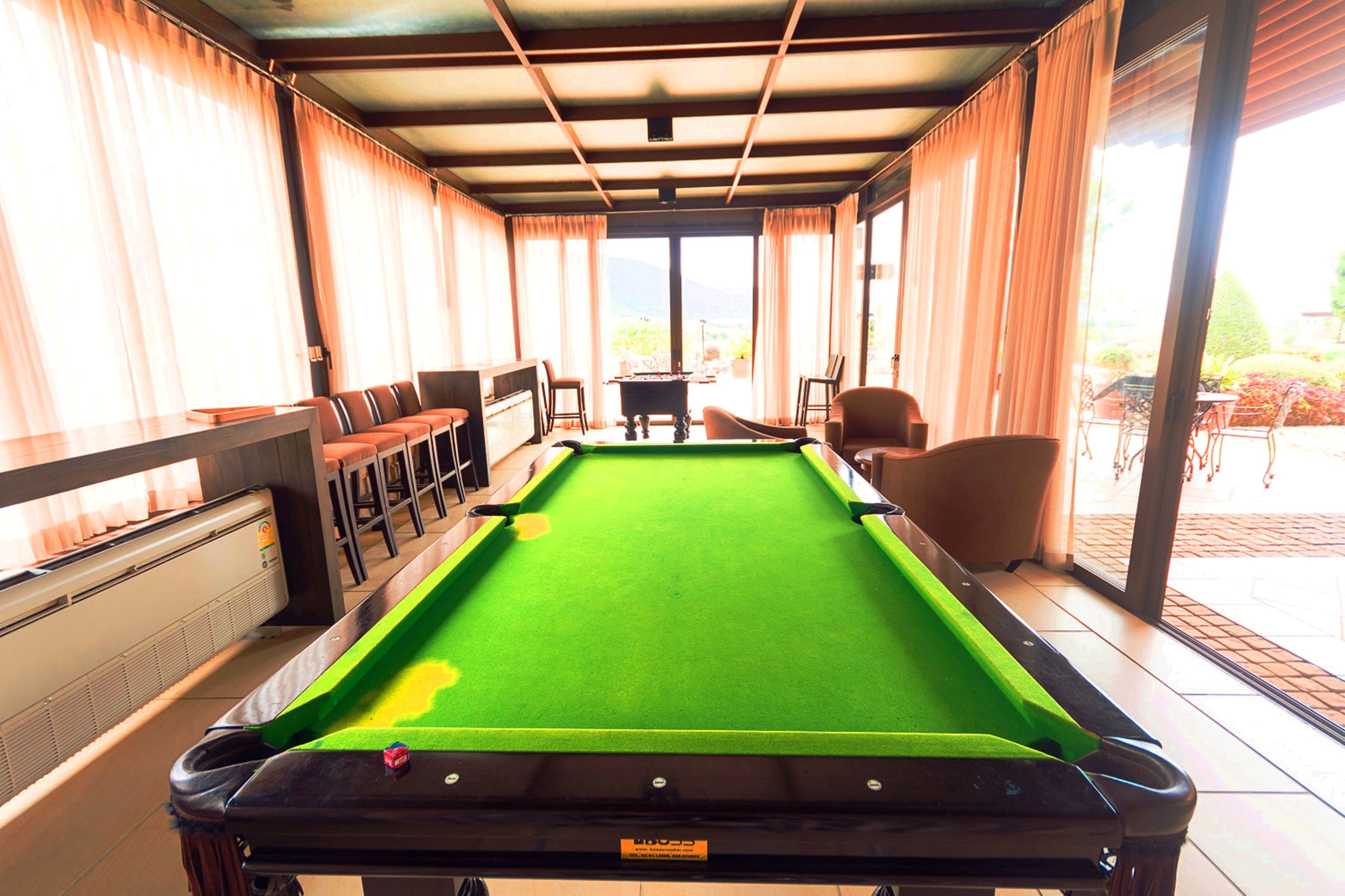 A pool table in a room with a view, cushioned seating, and a piano.