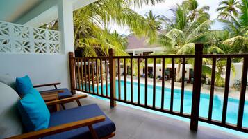 A balcony with a pool, wooden furniture, and palm trees.