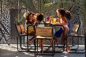 A group of children seated at a table with a wooden bench, surrounded by a perforated metal fence. - Casa Beach Hotel - Casa del Mar (Jambiani)