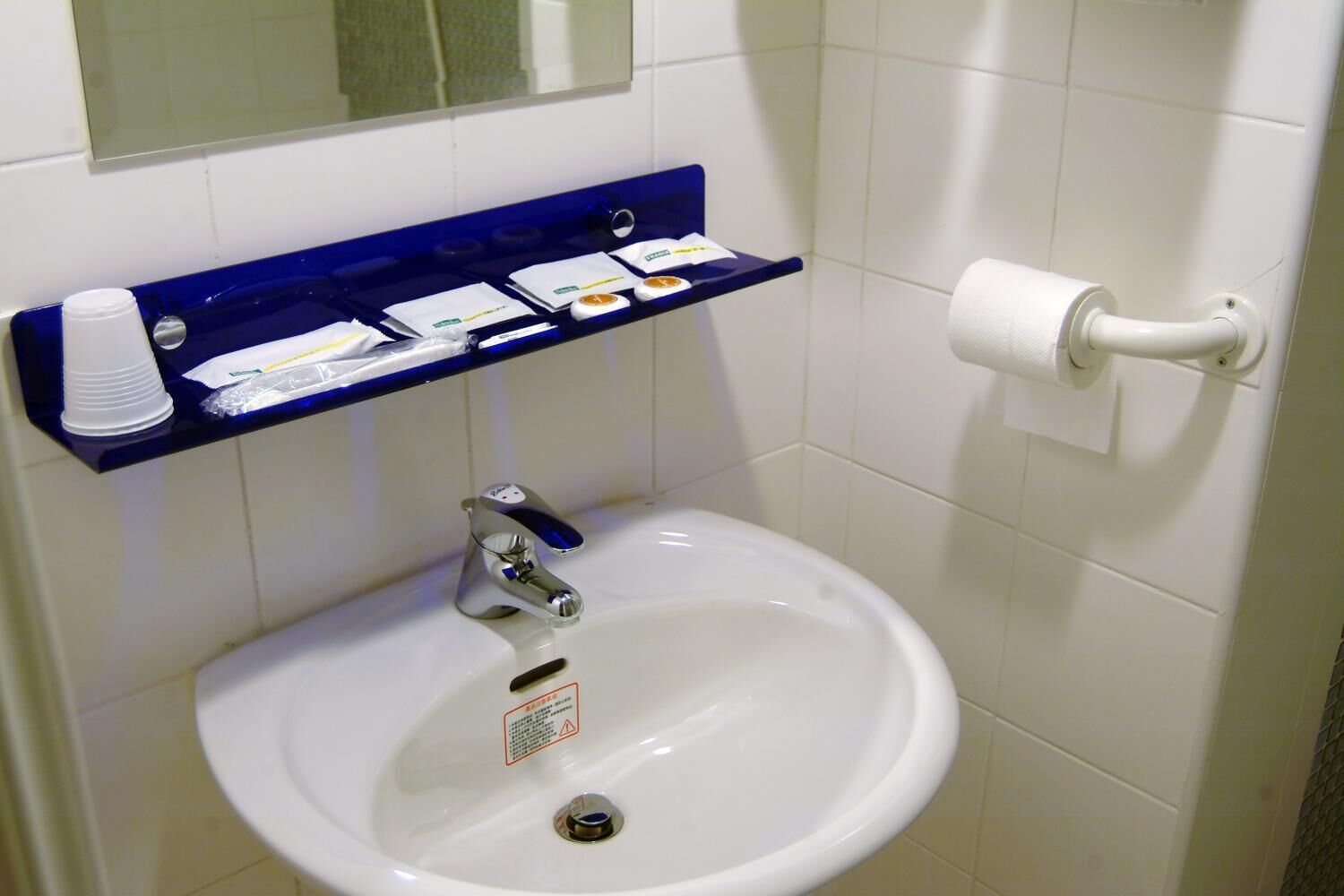 A bathroom with a white sink, a blue shelf with toiletries, and a toilet paper holder.