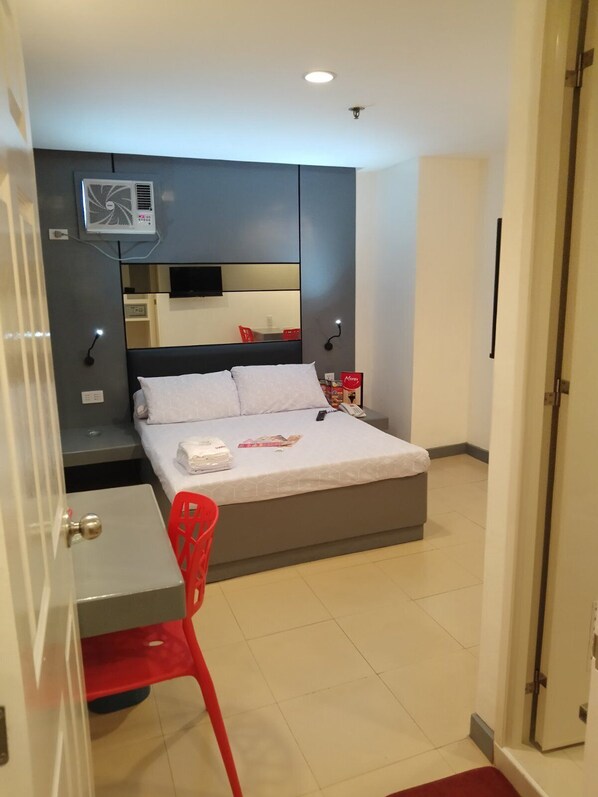 A modern hotel room with a bed, a desk, a chair, and a TV mounted on the wall.
