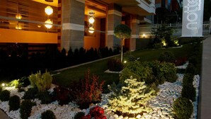 Entrada d'hotel ben il·luminada amb un disseny modern, amb un cartell ben visible i una zona de jardí paisatjística amb diverses plantes i un camí.